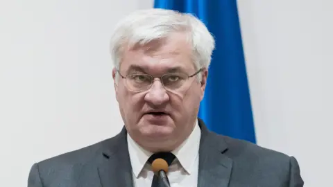Reuters Ukrainian Foreign Minister Andrii Sybiha speaks into a microphone. He has white hair and wears glasses. 