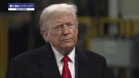 Donald Trump wears a red tie, white shirt and black coat.