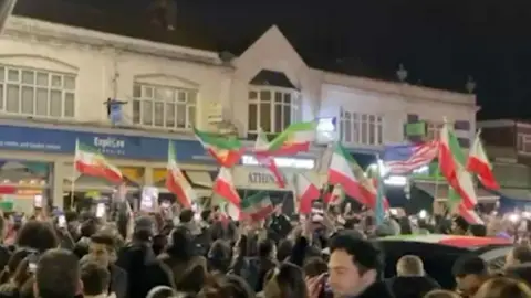 A crowd of people holding Iranian flags in a busy London street