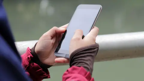 Getty Images Muslim Girl wearing religious dress and hijab using mobile phone at public park outdoor