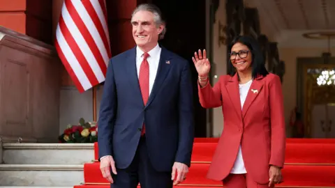 Reuters Venezuela's interim president, Delcy Rodriguez and US Interior Secretary Doug Burgum stand side by side smiling and Delcy Rodriguez waves