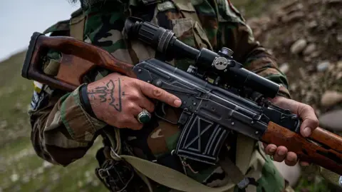 Getty Images A man in camouflage gear grips an assault rifle on a rocky hillside.