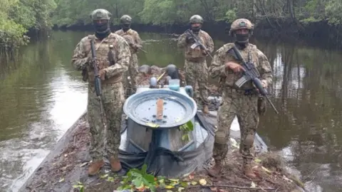 Ecuadorean Defence Ministry Four armed and uniformed members of the Ecuadoran military stand on top of a semi-submersible vessel in a mangrove-lined swamp.
